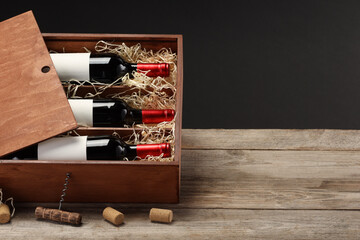 Canvas Print - Box with wine bottles, corkscrew and corks on wooden table against black background. Space for text