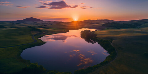 Wall Mural - A reflection photograph of a setting sun and orange sky reflected in a tranquil lake with rolling hills