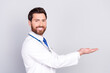 © deagreez - Profile portrait of experienced doctor man hold empty space wear white coat isolated on grey color background