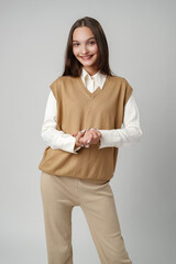 Wall Mural - Young Woman Wearing a Brown V-Neck Sweater Vest Over a White Shirt and Beige Pants