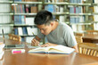 © Pormezz - male asian student studying and reading book in library