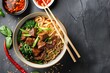 © ylivdesign - Bowl of beef noodle soup with chopsticks, fresh herbs, and spices on dark stone background
