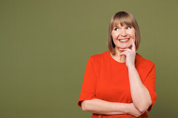 Wall Mural - Elderly blonde woman 50s years old she wear orange t-shirt casual clothes put hand prop up on chin, lost in thought and conjectures isolated on plain pastel green background studio. Lifestyle concept.