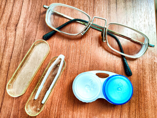 Close-up of eyeglasses, contact lens case, and tweezers on a wooden surface