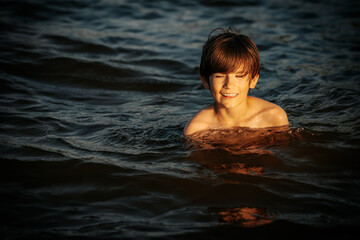 A boy swimming in the ocean, smiling and flashing a peace sign with his fingers. The image captures a joyful and carefree moment during a summer day at the beach