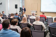 © Anton Gvozdikov - Attendees listening to presentation during a business conference in an auditorium. Speaker and camera recording in background