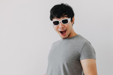 Funny acting and wow face of asian man wearing gray and fashion white sunglasses, standing isolated over white background wall.