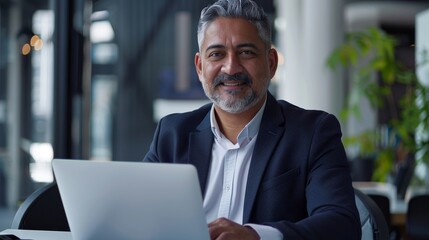 Poster - A successful businessman, smiling confidently, works on his laptop in a modern office setting. He represents professionalism, success, and digital technology.