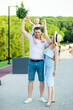© Any Grant - happy young parents mom and dad are walking with a baby in a stroller in the park in a hat in the summer in the setting sun and smiling having fun