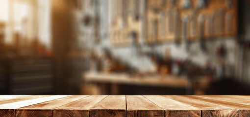 Wall Mural - Empty wooden work table with space for tools and products. Blurred background of craft workshop and wall with tools.