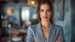 © aicandy - A confident young woman dressed in a stylish grey blazer stands with arms crossed in a contemporary indoor setting, exuding professionalism and self-assurance