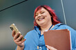 © LIGHTFIELD STUDIOS - A plus size woman with bright pink hair laughs while looking at her phone.