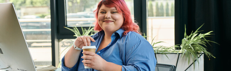 A plus size businesswoman with pink hair sips coffee while sitting at a desk in a modern office.