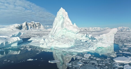 Wall Mural - Melting iceberg peacefully floats in the ocean. Ice floe reflecting in crystal ocean water drifts in Antarctica. Towering glacier under blue sky. Ecology, climate change global warming, close up