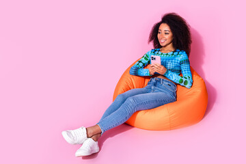 Sticker - Full size photo of lovely young lady sit orange beanbag hold device dressed stylish blue garment isolated on pink color background