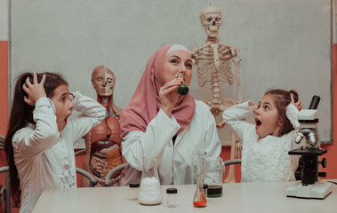 Wall Mural - Kids scientists with a female Muslim teacher have fun while doing chemistry science experiments in the school lab. 