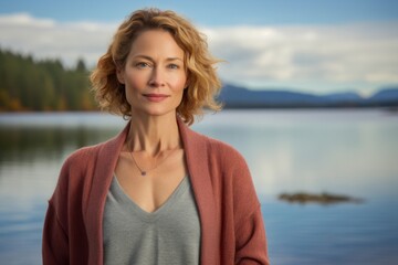 Canvas Print - Portrait of a content woman in her 40s wearing a chic cardigan while standing against serene lakeside view