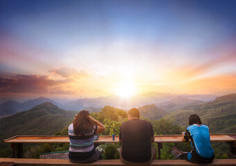 Wall Mural - asian couple looking at sunset on the top of the mountain, travel concept