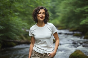 Wall Mural - Portrait of a jovial woman in her 30s sporting a vintage band t-shirt while standing against tranquil forest stream