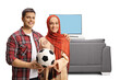© Ljupco Smokovski - Young man and a muslim woman holding a football in front of tv