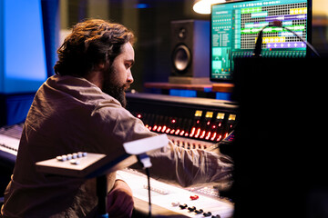 Fototapete - Audio technician working on recording and editing new music in studio, processing sounds by using mixing console and twisting knobs in control room. Sound producer pushing buttons and sliders.