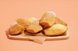 © Pixel-Shot - Wooden board with delicious madeleines and powdered sugar on orange background