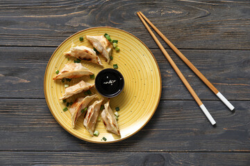 Wall Mural - Plate with fried Japanese gyoza and bowl of soy sauce on black wooden background