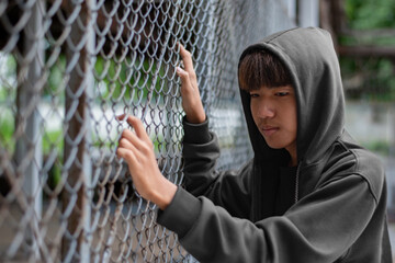 asian preteen boy in a black hoodie holding a metal fence panel in a juvenile detention facility, aw