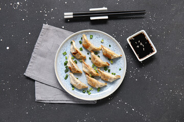 Wall Mural - Plate with fried Japanese gyoza and bowl of soy sauce on black background