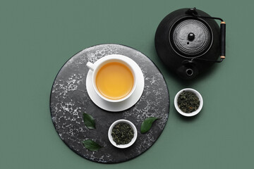 Poster - Cup and teapot of hot tea with dried leaves on green background