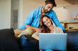 © Penn/peopleimages.com - Couple, laptop and happy on sofa in home with social media scroll, relax and watching movie with bonding. People, technology and smile on couch in living room with online streaming and affection