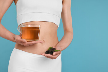 Poster - Weight loss concept. Woman with cup of diet tea and dry leaves on light blue background, closeup