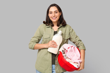 Canvas Print - Young woman with laundry basket and bottle of detergent on grey background