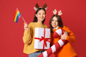 Poster - Young lesbian couple with LGBT flag, Christmas gift and candy cane pillow on red background