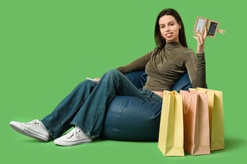 Canvas Print - Young woman with credit card holder and shopping bags sitting on chair against green background