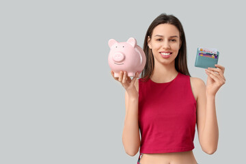 Poster - Young woman with credit card holder and piggy bank on grey background