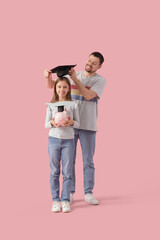 Poster - Father putting mortar board on his daughter with piggy bank on pink background. Tuition fees concept