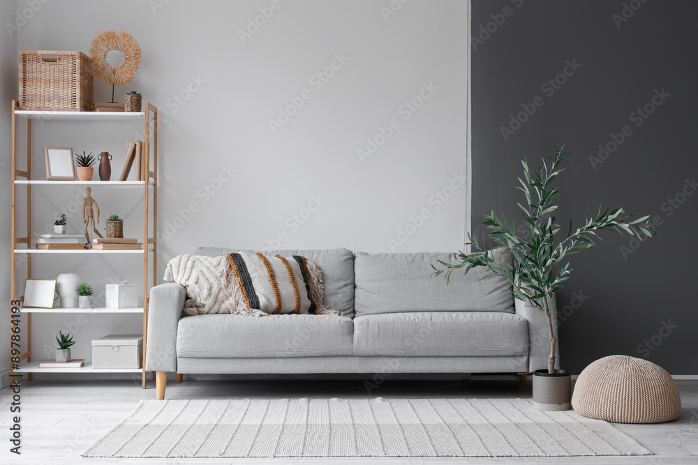 Comfortable sofa with cushions, shelving unit, pouf and decorative olive tree