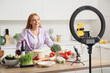 © Pixel-Shot - Mature woman with tasty food recording video class in kitchen
