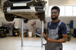 © sofiko14 - Mechanic inspecting car on hydraulic lift in auto repair shop. Man in overalls standing with clipboard in hand, ready for maintenance tasks. Professional automotive service environment.
