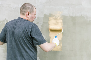 Wall Mural - A man is painting a wall with a roller