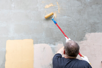 Wall Mural - A man is painting a wall with a roller