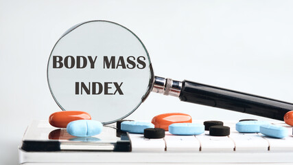 Wall Mural - Business concept acronym. BMI. Body Mass Index through a magnifying glass on a calculator with tablets on a gray background. The concept of medicine