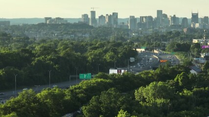 Wall Mural - Nashville city skyline with lush green forest and busy highway at sunset, aerial view