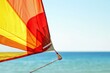© Aksana - Vibrant colorful kite flying by the beach, red and yellow kite against blue sky and ocean, recreational activity, summer leisure concept