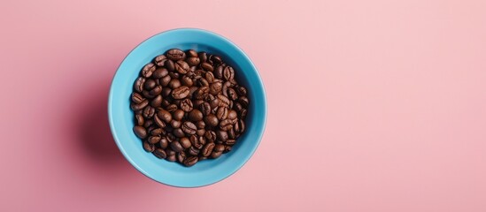 Wall Mural - View from above of a blue cup filled with coffee beans on a pink background surrounded by copy space Breakfast and coffee concept with a closeup of the beans emphasizing a cafe morning ambiance