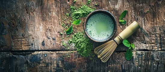 Poster - Top down view of a fresh matcha tea cup with a bamboo whisk and green powder on a wooden surface providing ample copy space image