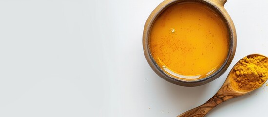 Poster - Top view of a ceramic cup filled with hot Turmeric tea beside a wooden spoon holding turmeric powder displayed on a white background for a health conscious immune boosting concept with a copy space im