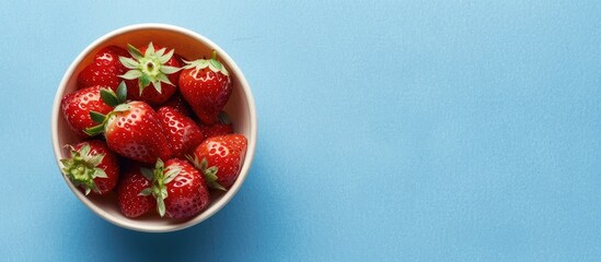 Poster - Delicious berry dessert featuring fresh ripe strawberries in a cup on a blue paper background viewed from the top with copy space image