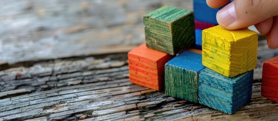 Poster - Colorful wooden building blocks and a cube for an educational concept with a hand holding a wooden block arranged with a copy space image